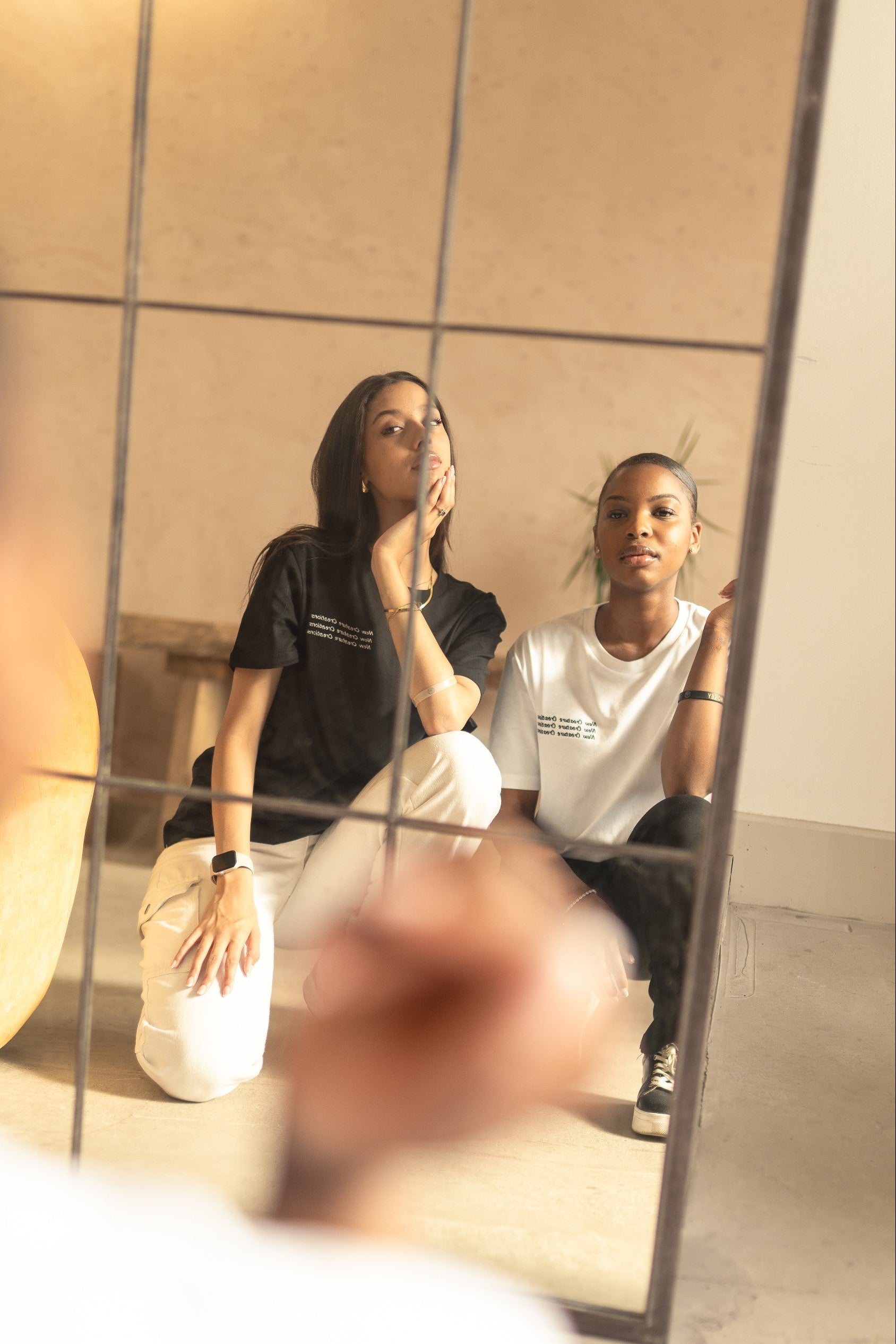 Two women sitting on a couch with a mirror between them reflecting their images.